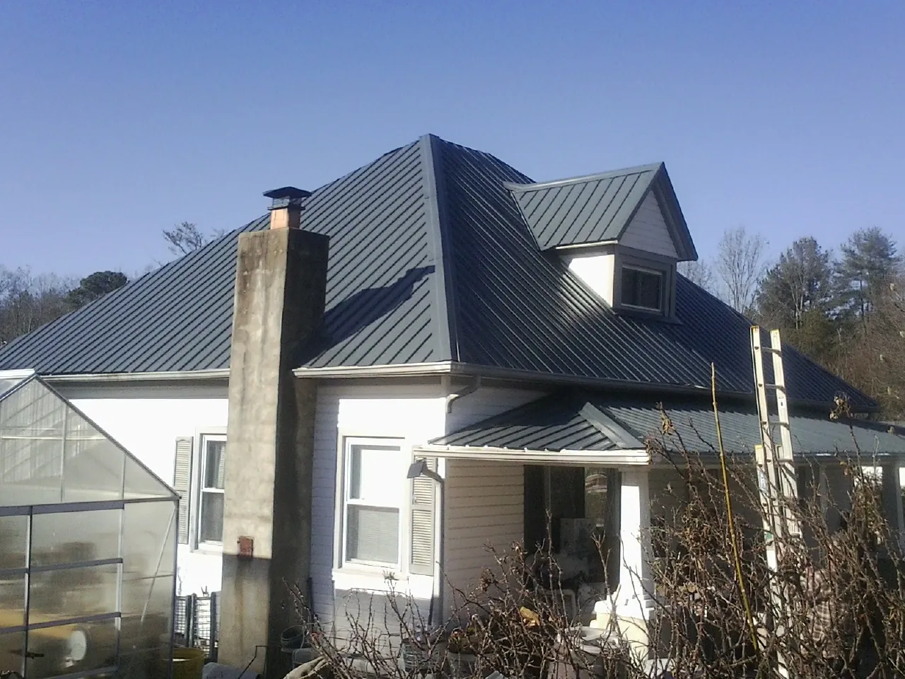 Dark blue standing seam metal roof on a white farmhouse with dormer — Slate & Tile Roof Repair by Roofing Brothers in Newport Beach