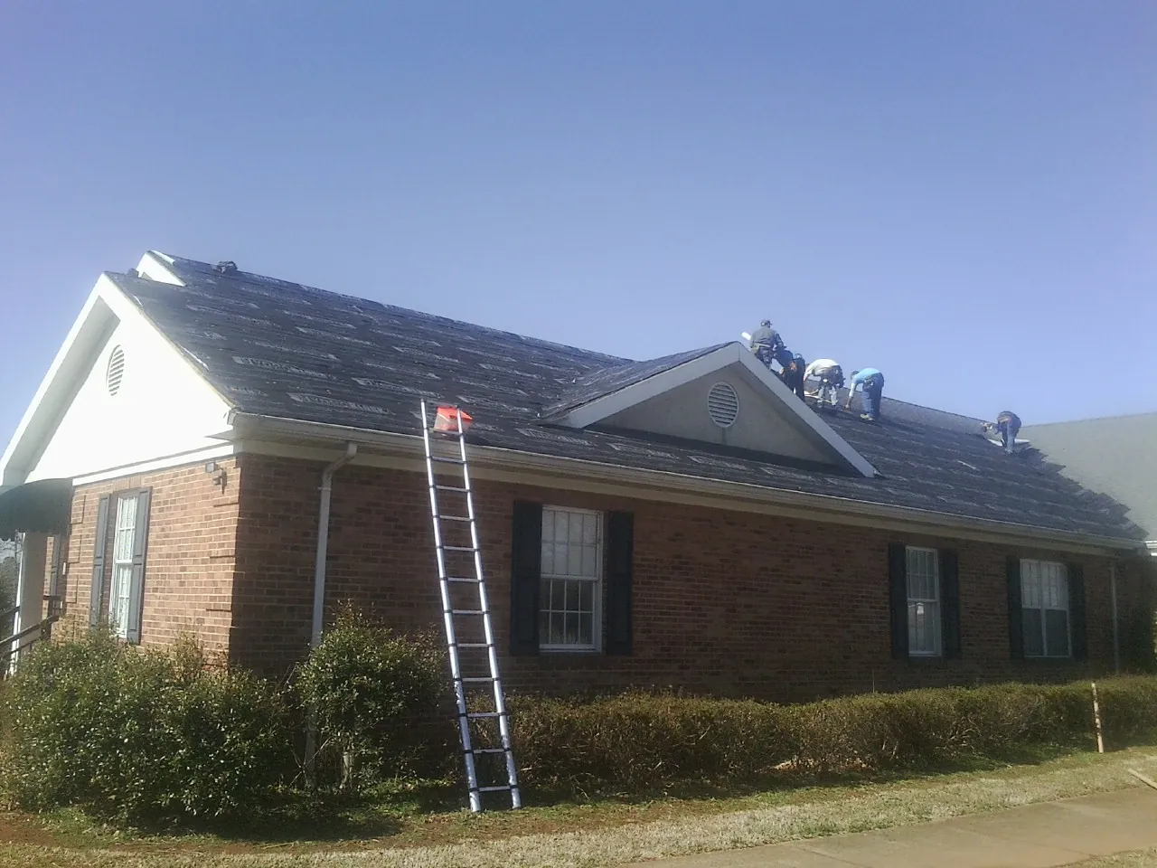 Crew tearing shingles off a brick ranch roof with a ladder set — Emergency Roof Repair work by our crew in Newport Beach