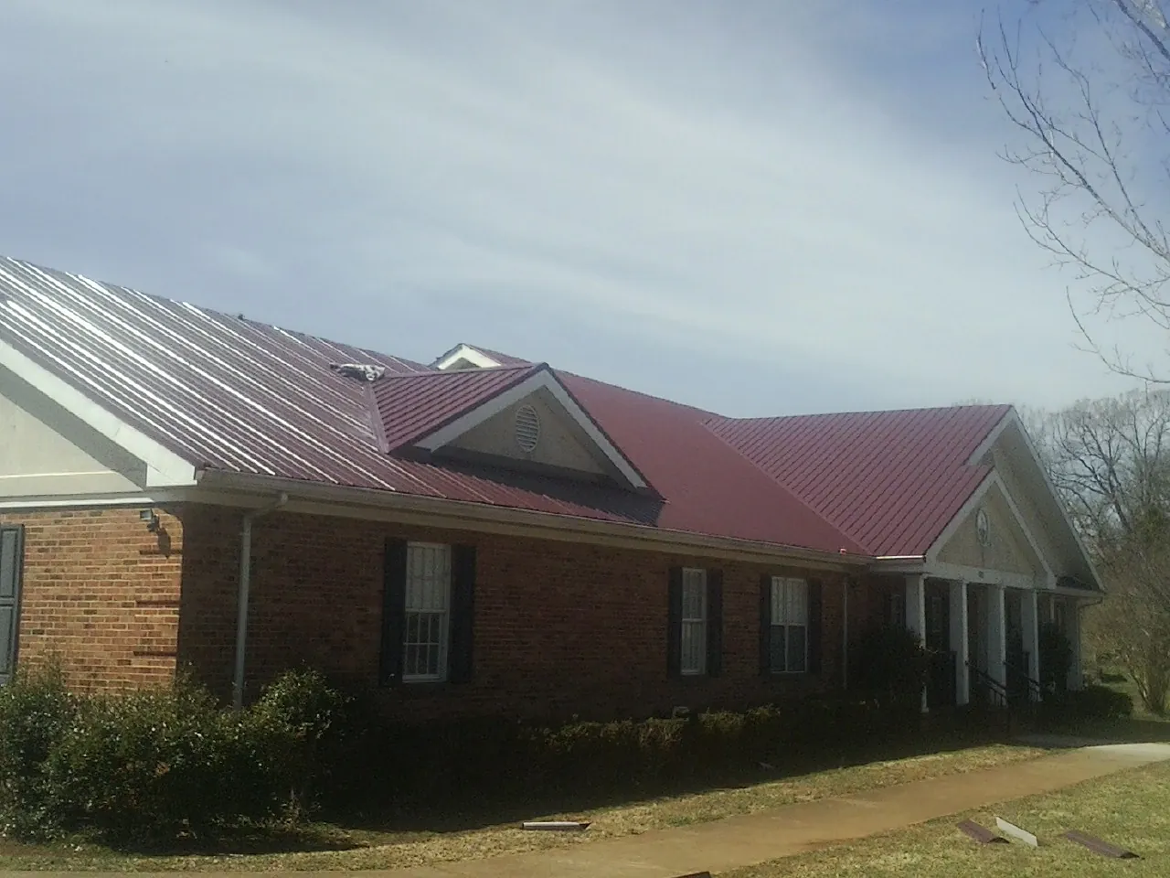 Red metal roof with gabled entries on a long brick building, from a Hail Damage Roof Repair job in Newport Beach