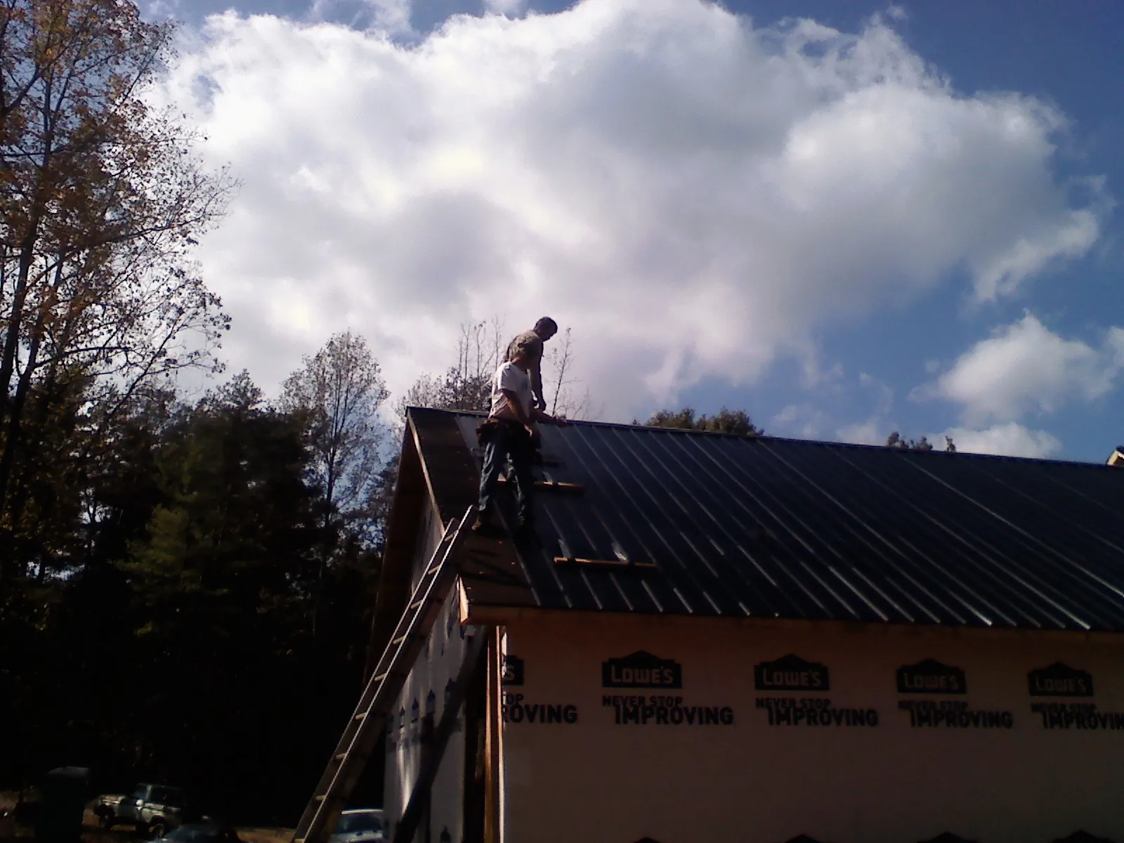 Roofer fastening dark metal panels high against a cloudy sky, from a Roof Inspection job in Newport Beach