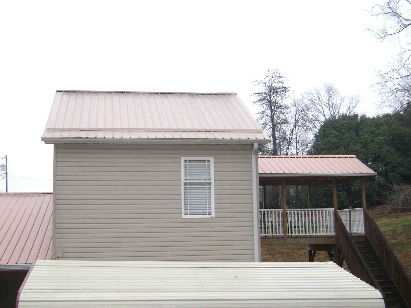 Tan metal roofs on a two story addition and attached porch, from a Roof Replacement job in Newport Beach